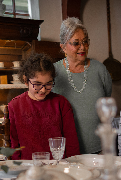 Een oma kijkt met haar kleinkind naar de gedekte tafel in de Achterkamer van de Oudheidkamer.