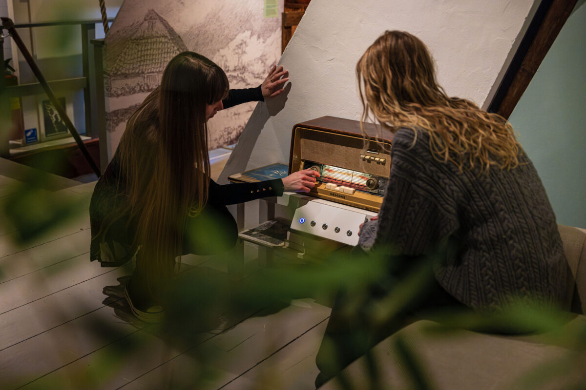 Nieuwe tentoonstelling boven de bank bij de Oudheidkamer. Twee dames kijkend naar een oude radio