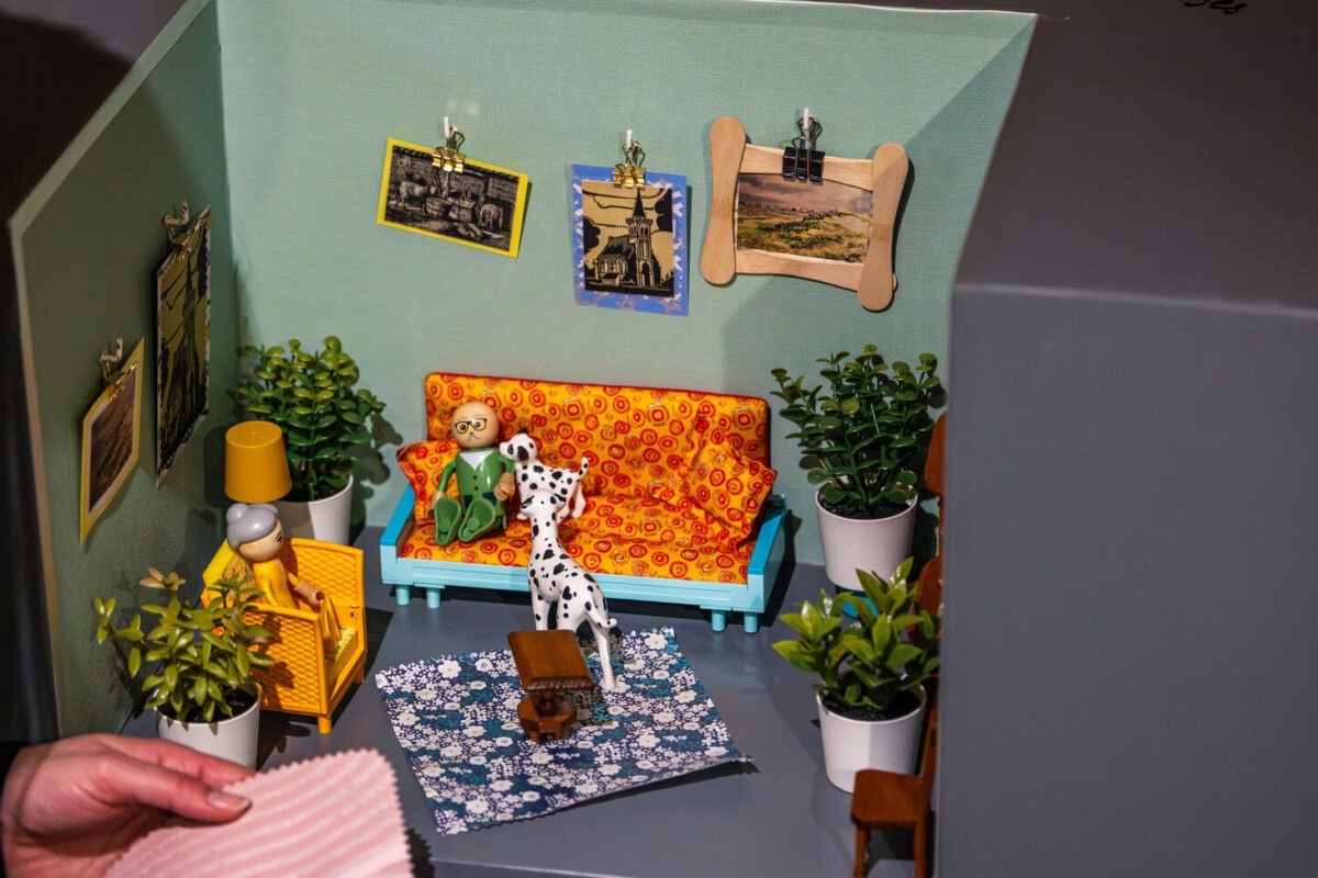 Een hand houdt een lapje vast voor een ingerichte poppenhuiskamer.